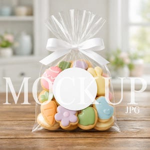 May include: A clear cellophane bag tied with a white ribbon, filled with colorful Easter-themed cookies. The cookies are shaped like eggs, carrots, flowers, bunnies, and birds. The word "MOCK UP" is printed on the bag.