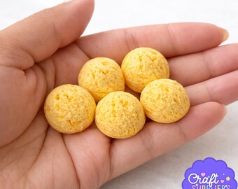 Könnte beinhalten: Sechs kleine, runde, gelbe Bastelperlen mit strukturierter Oberfläche werden in einer Hand gehalten. Die Perlen haben eine helle, goldgelbe Farbe. Ein lila Logo mit dem Text "Craft Supplier's Co." befindet sich in der unteren rechten Ecke.