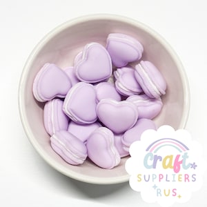 Op de afbeelding: Een kom gevuld met lavendelkleurige hartvormige macarons. De macarons hebben een witte vulling en zijn in een willekeurig patroon gerangschikt.
