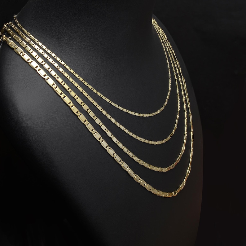 May include: Four gold-colored necklaces displayed on a black mannequin. Each necklace features a delicate, rectangular link design. The necklaces vary in length, creating a layered effect. The chains are presented against a dark background.