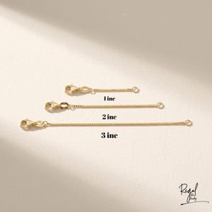 May include: Three gold-colored chain extenders, each with a lobster clasp and a small ring. The extenders are labeled with their lengths: 1 inch, 2 inches, and 3 inches. The background is a neutral beige.