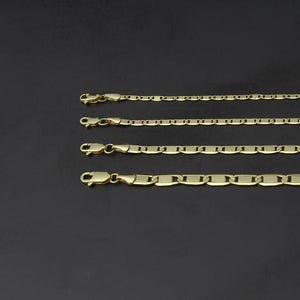 May include: Four gold-colored chain necklaces of varying styles and thicknesses are displayed against a dark background. Each chain features a clasp at one end. The chains are arranged parallel to each other, showcasing their different link designs.