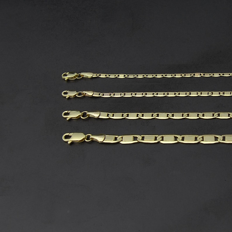 May include: Four gold-colored chain necklaces of varying styles and thicknesses are displayed against a dark background. Each chain features a clasp at one end. The chains are arranged parallel to each other, showcasing their different link designs.