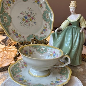 May include: A vintage teacup and saucer set with a delicate floral pattern in shades of pink, yellow, and blue. The set features a green and gold trim and a scalloped edge.