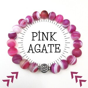 May include: Pink agate bracelet with white stripes and a silver charm. The bracelet is made of natural stones and is a beautiful and unique piece of jewelry.