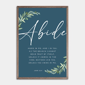 Op de afbeelding: Een ingelijste print met het woord "Abide" in elegant wit schrift. De teal achtergrond bevat tekst uit Johannes 15:4, met olijftak accenten. De houten lijst voegt een rustieke touch toe aan deze inspirerende wandkunst.