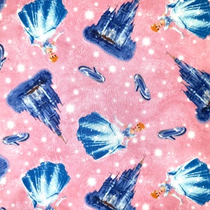 May include: A pink fabric with a repeating pattern of Cinderella, her glass slipper, and Cinderella's castle. The castle is blue and white and the slipper is blue.
