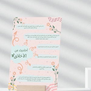 Peut inclure: Une affiche aux couleurs pastel avec du texte arabe et des motifs floraux, présentée sur un bloc de bois. L'affiche présente de la calligraphie et des illustrations, probablement liées à des enseignements ou des citations islamiques. Le design est doux et invitant.