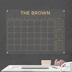 Acrylic family calendar with gold hardware and gold lettering, including sections for monthly planning, notes, tasks, and menu.