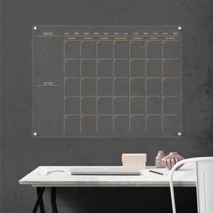 Acrylic wall calendar with gold hardware and gold writing, with a full monthly layout, sections for notes, and to-do on the left side.