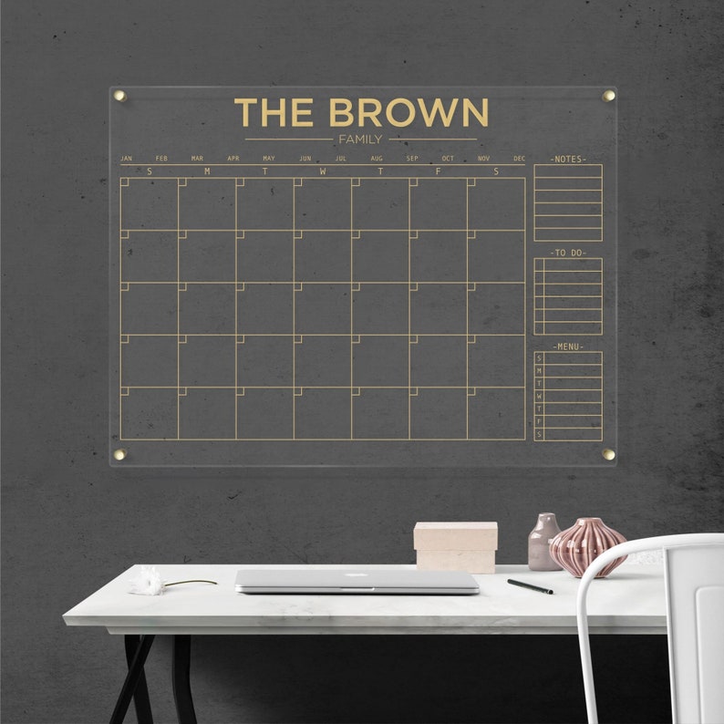 Acrylic family calendar with gold hardware and gold lettering, including sections for monthly planning, notes, tasks, and menu.