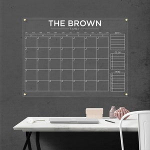 Acrylic family calendar with gold hardware and white lettering, including sections for monthly planning, notes, tasks, and menu.