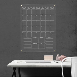 Featuring a monthly layout, notes, a menu section, and personalized spaces for four name boxes. Clear acrylic wall calendar with gold hardware and white text.