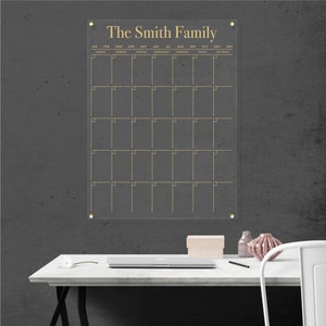 Customized acrylic wall calendar with gold writing, mounted with gold hardware.