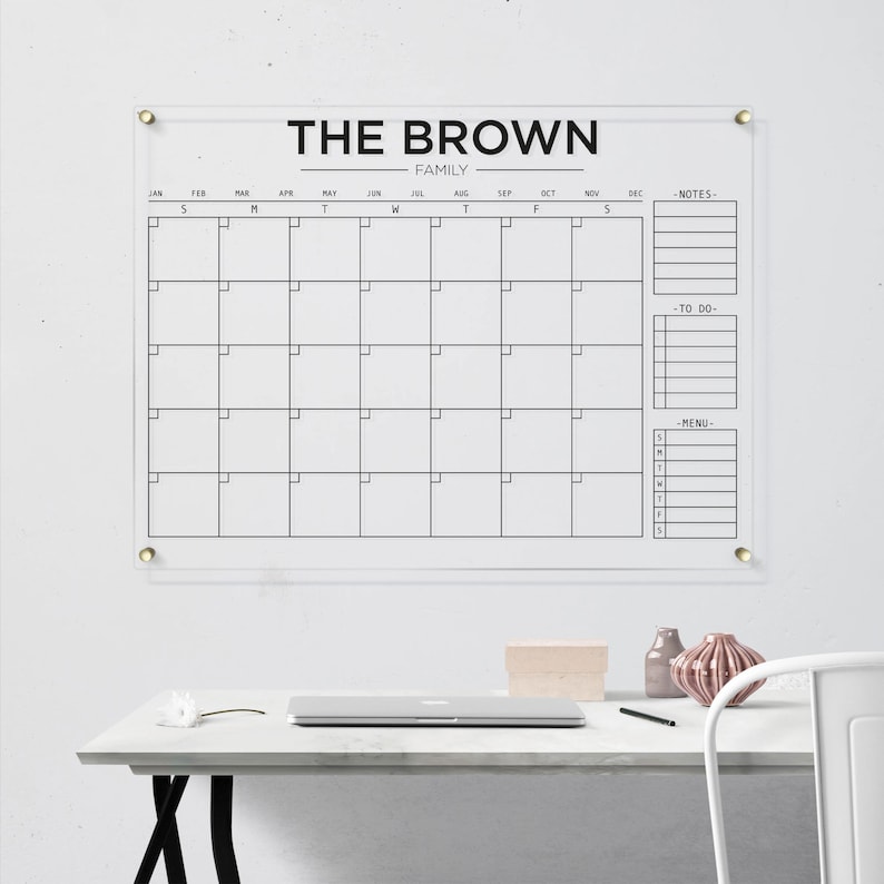 Acrylic family calendar with gold hardware and black lettering, including sections for monthly planning, notes, tasks, and menu.