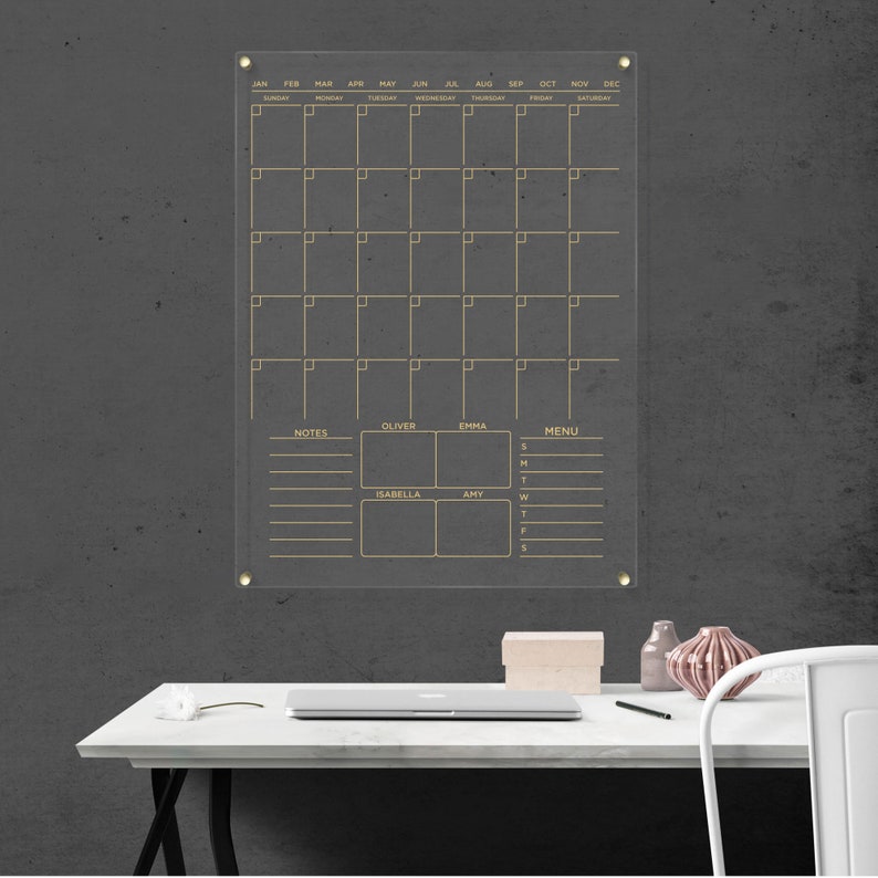 Featuring a monthly layout, notes, a menu section, and personalized spaces for four name boxes. Clear acrylic wall calendar with gold hardware and gold text.