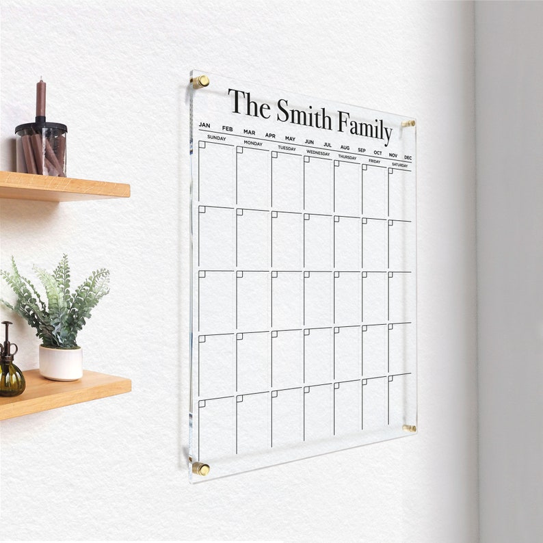 Customized acrylic wall calendar with black writing, mounted with gold hardware.