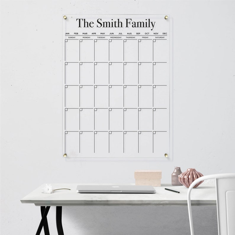 Customized acrylic wall calendar with black writing, mounted with gold hardware.