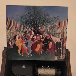 May include: A dark brown wooden music box with a hinged lid displaying a painting of a lively outdoor dance scene. The box has floral patterns. The internal mechanism of the music box is visible.