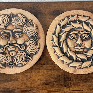 May include: Two round, tan-colored ceramic wall plaques with embossed faces. One features a bearded face with flowing hair, the other a face surrounded by leaves. Decorative art for home decor.