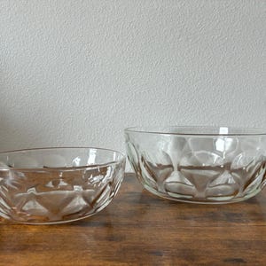 May include: Two clear glass bowls of different sizes, each featuring a repeating geometric pattern of circular indentations around the exterior. The bowls have smooth, rounded rims and a transparent finish, showcasing a consistent design style.