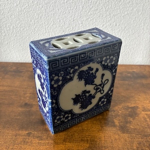 May include: A rectangular blue and white ceramic vase with a floral and cloud design. The vase has a rectangular shape with a series of holes on the top. The vase is decorated with a repeating geometric pattern.