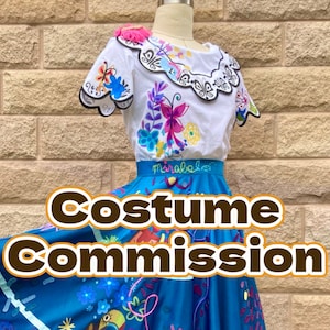 May include: A blue and white skirt with colorful floral embroidery and a white blouse with a scalloped collar and floral embroidery. The text "Costume Commission" is superimposed on the image.