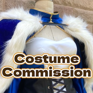 Puede incluir: Una capa de terciopelo azul con ribete de piel blanca. La capa se lleva sobre un top blanco sin tirantes y un corsé negro. El texto "Costume Commission" se superpone a la imagen.