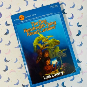 May include: A blue paperback book titled "The One Hundredth Thing About Caroline" by Lois Lowry. The cover features an illustration of three children and dinosaurs.