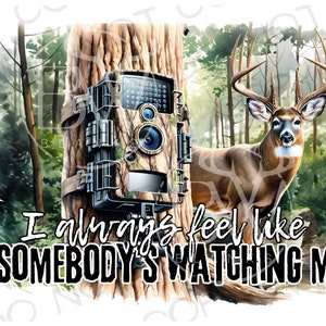 Puede incluir: Una cámara de seguimiento de camuflaje montada en un tronco de árbol en un entorno boscoso. Un ciervo de cola blanca se encuentra en el fondo. El texto "I always feel like somebody's watching me" está escrito debajo de la cámara.