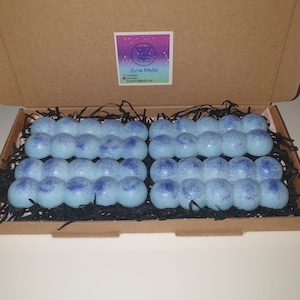 Könnte beinhalten: Ein Karton mit vier Sets hellblauer, blasenformiger Wachsschmelzen. Jedes Set hat ein dunkleres blau gesprenkeltes Design. Die Box enthält auch einen Aufkleber mit dem Text "Zuna Meltz" und Kontaktinformationen.