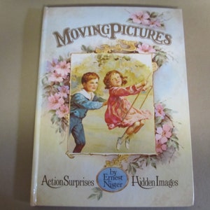 May include: A vintage children's book titled "Moving Pictures" by Ernest Nister. The cover features a colorful illustration of two children on a swing set with pink flowers surrounding the image. The book includes "Action Surprises" and "Hidden Images".