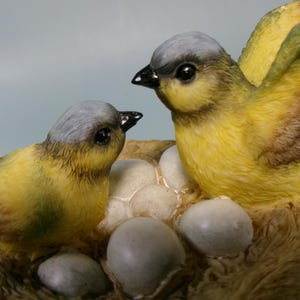 Peut inclure: Figurine d&eacute;taill&eacute;e de deux oiseaux jaunes et gris avec des becs noirs, perch&eacute;s pr&egrave;s d'un nid avec plusieurs &oelig;ufs. Un oiseau a les ailes d&eacute;ploy&eacute;es. Le nid est fait d'un mat&eacute;riau brun clair.