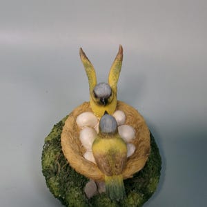 Peut inclure: Figurine d&eacute;taill&eacute;e de deux oiseaux jaunes et gris dans un nid avec des &oelig;ufs blancs. Le nid est fait de mat&eacute;riau couleur paille et repose sur une base de mousse verte. Les oiseaux ont une apparence r&eacute;aliste et d&eacute;taill&eacute;e.