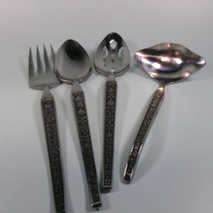 May include: A set of four silver-toned serving utensils: a fork, two spoons, and a ladle. Each piece has a decorative floral pattern on the handle. The utensils are arranged on a light blue surface.