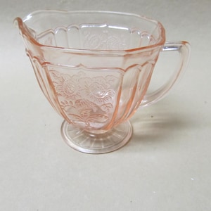 May include: A pink glass creamer with a floral design and a footed base.