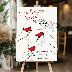 May include: White sign with black calligraphy that reads "Vino before Vows" and "Let's celebrate Amelia's Bridal Shower". The sign features a hand pouring wine from a bottle into a glass, and three other hands holding glasses of red wine.