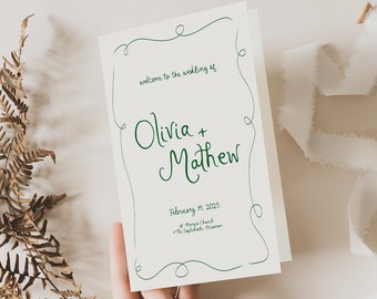 Puede incluir: Un programa de boda con escritura verde que dice "bienvenida a la boda de Olivia + Mathew" y la fecha 19 de febrero de 2025. El programa se sostiene en una mano, con un helecho seco y una cinta blanca en el fondo.