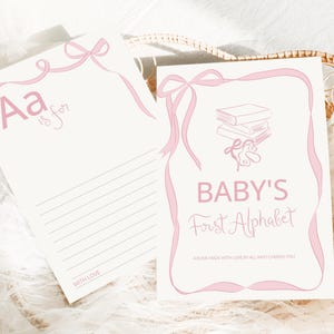 Puede incluir: Dos tarjetas de alfabeto para bebés con lazos rosas. Una tarjeta dice "Aa is for" con líneas. La otra tarjeta dice "Baby's First Alphabet" con una pila de libros y una ilustración de oso de peluche.