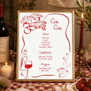 May include: A gold-framed menu sign featuring red line art illustrations of tomatoes, a wine bottle, a glass, and pasta shapes. The text reads Cin Cin, Wine, Prosecco, Chianti, Chardonnay, Sangiovese, Sauvignon Blanc, Cocktails, Espresso Martini, Limoncello Spritz, Acqua, sparkling water, and still water.
