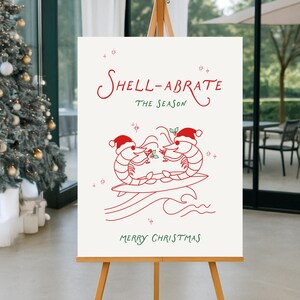 May include: A white sign on a wooden easel with red and green text and illustrations. The text reads "Shell-abrate the Season" and "Merry Christmas." Two shrimp wearing Santa hats are illustrated holding cocktails. The sign is in front of a Christmas tree.
