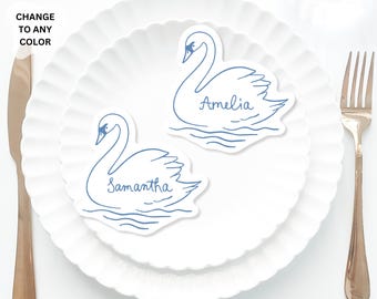 May include: Two swan-shaped place cards with names Amelia and Samantha, in blue ink, rest on a white plate. A knife and fork are on either side. The text "CHANGE TO ANY COLOR" and "max 5inch" are also visible.