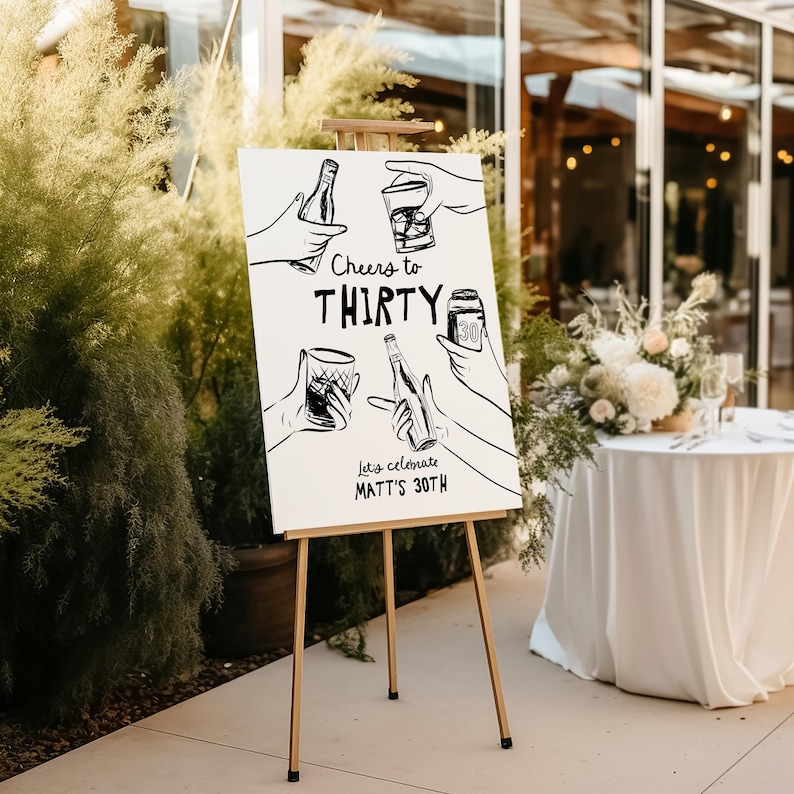 May include: White sign with black hand-drawn illustrations of people raising glasses and bottles, with the text "Cheers to Thirty" and "Let's celebrate Matt's 30th".