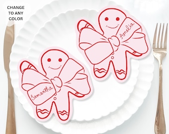 May include: Two red gingerbread person place cards with pink bows and the names Amelia and Samantha written on them. The place cards are on a white plate.