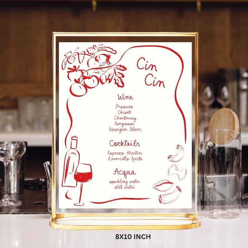 May include: A vertical 8x10 inch menu sign in a gold metal frame. The white card features red line drawings of tomatoes, a wine bottle, a glass, and pasta shapes. Text includes Cin Cin, Wine, Prosecco, Chianti, Chardonnay, Sangiovese, Sauvignon Blanc, Cocktails, Espresso Martini, Limoncello Spritz, Acqua, sparkling water, and still water.