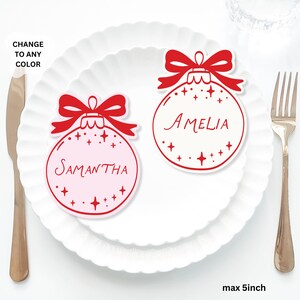 May include: Two Christmas ornament-shaped place cards with red bows and star accents. One is light pink with the name "Samantha", the other is white with "Amelia". The text "CHANGE TO ANY COLOR" is in the upper left corner. The maximum size is 5 inches.