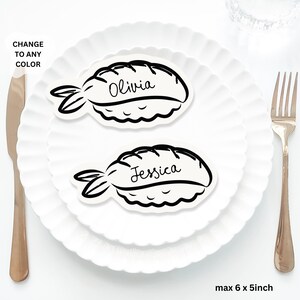 May include: Two white sushi-shaped place cards with black outlines, each bearing a name in cursive: "Olivia" and "Jessica." The cards rest on white plates, with a fork and knife visible. Text in the image reads "CHANGE TO ANY COLOR" and "max 15 x 13cm."
