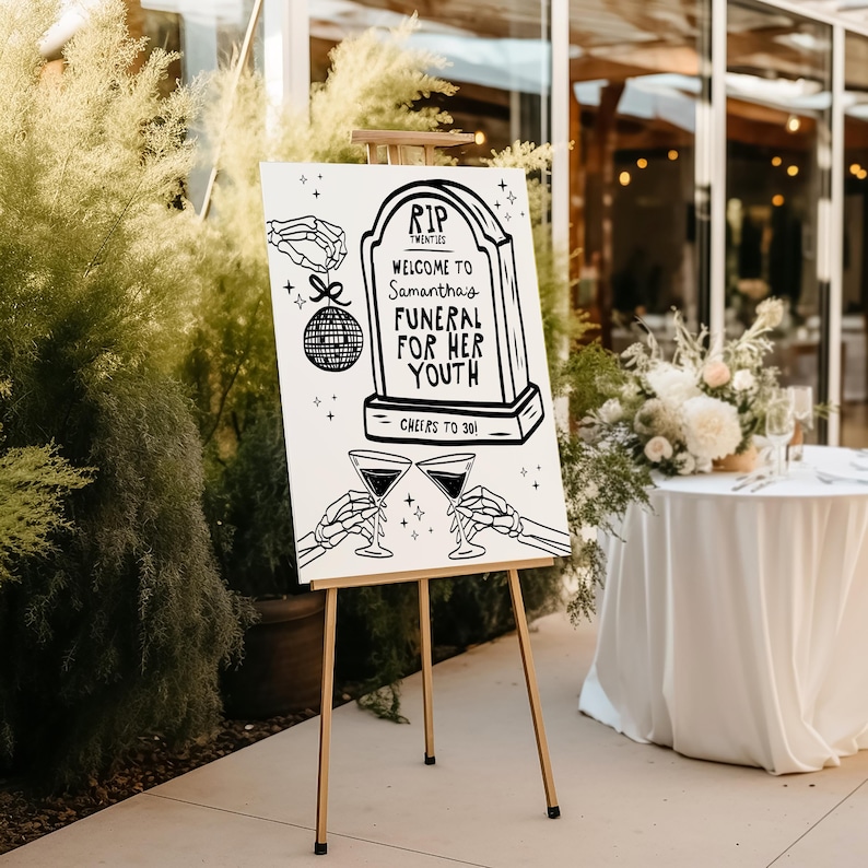 May include: A white sign on an easel with black text that reads "RIP Twenties Welcome to Samantha's Funeral for her Youth Cheers to 30!" The sign features a tombstone with a disco ball hanging from it.