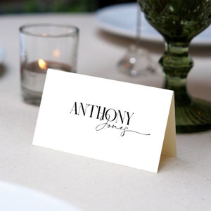 May include: White place card with black text that reads "ANTHONY Jones" in a cursive font.