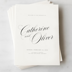 May include: A stack of white rectangular wedding programs with black text. The text reads: WELCOME TO THE WEDDING OF, Catherine and Oliver, SUNDAY, FEBRUARY 14, 2024, ST MARY'S CHURCH, 134 THE ESPLANADE, MOSMAN. The names are in a large, elegant script font.